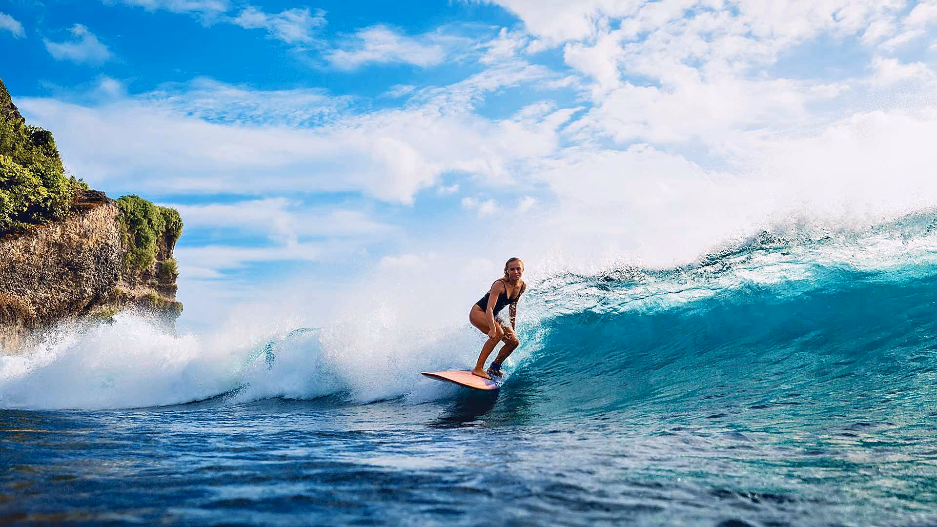 Studentin surft eine Welle auf Bali