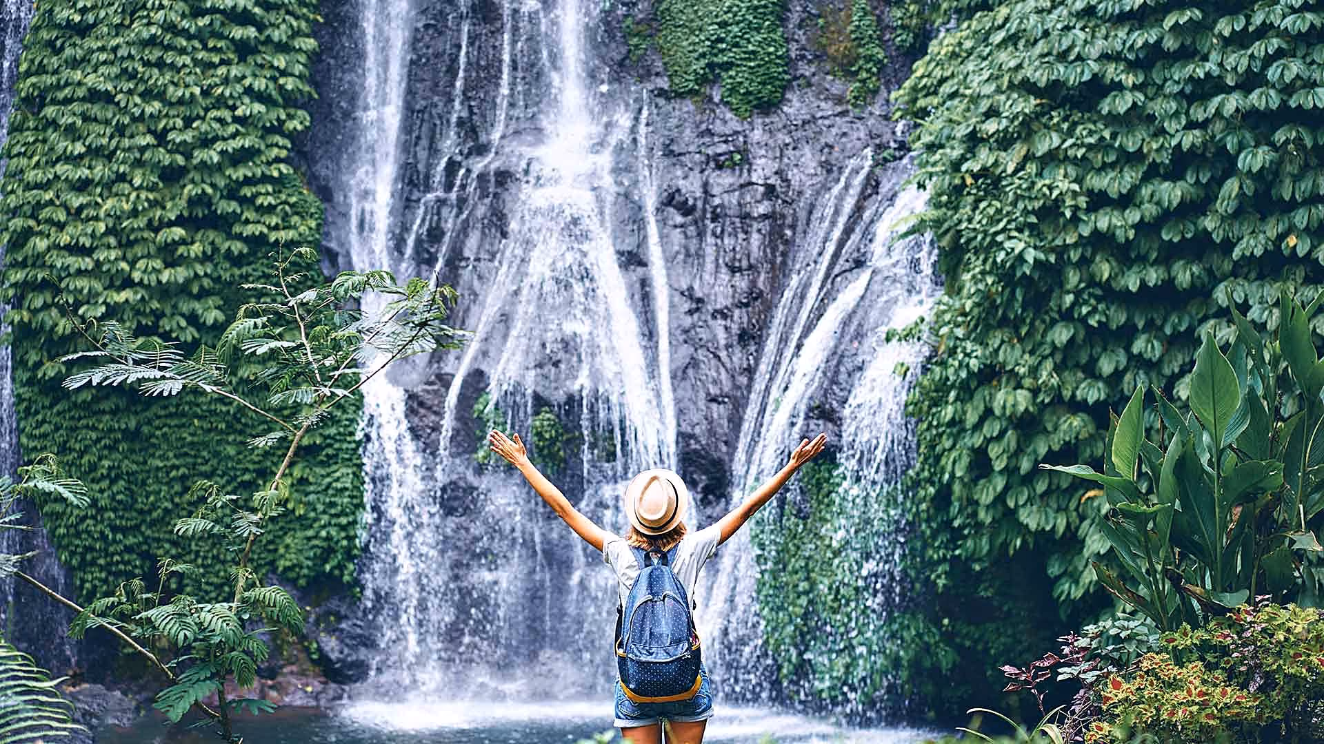 Studentin mit ausgebreiteten Armen vor einem Wasserfall auf Bali
